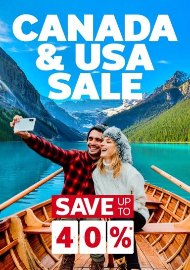 Canada & USA sale | save up to 40%*. Couple taking a selfie in a rowboat with snowy mountains and pine trees in the background