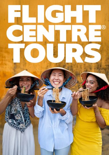 Flight Centre Tours - three women smiling, eating noodles in front of a yellow wall