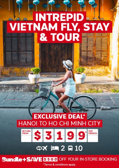 Intrepid Vietnam fly, stay & tour | Exclusive deal* Return from $3,199* per person. Woman on a bike riding past yellow buildings in Vietnam