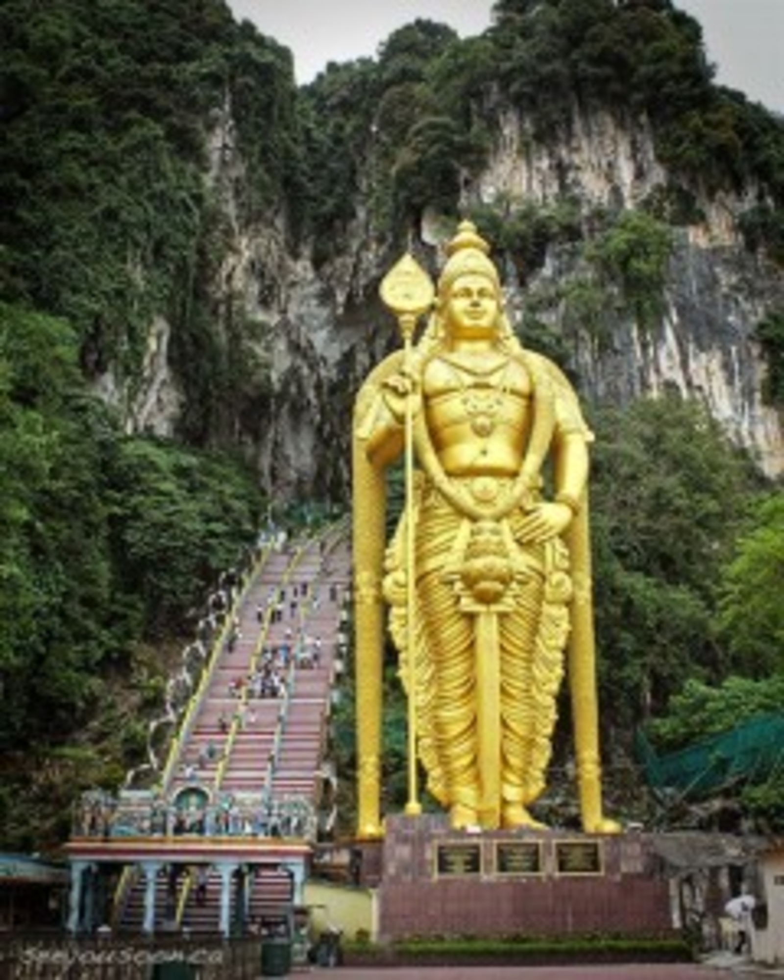 Gold statue of Lord Murugan in front of stairs leading up into the Batu Caves Temple