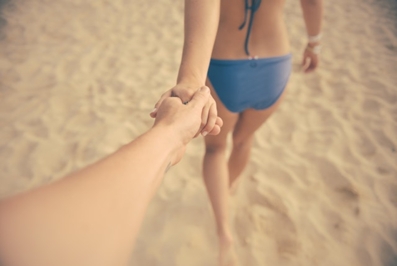 Arm being led down the beach by person in bikini