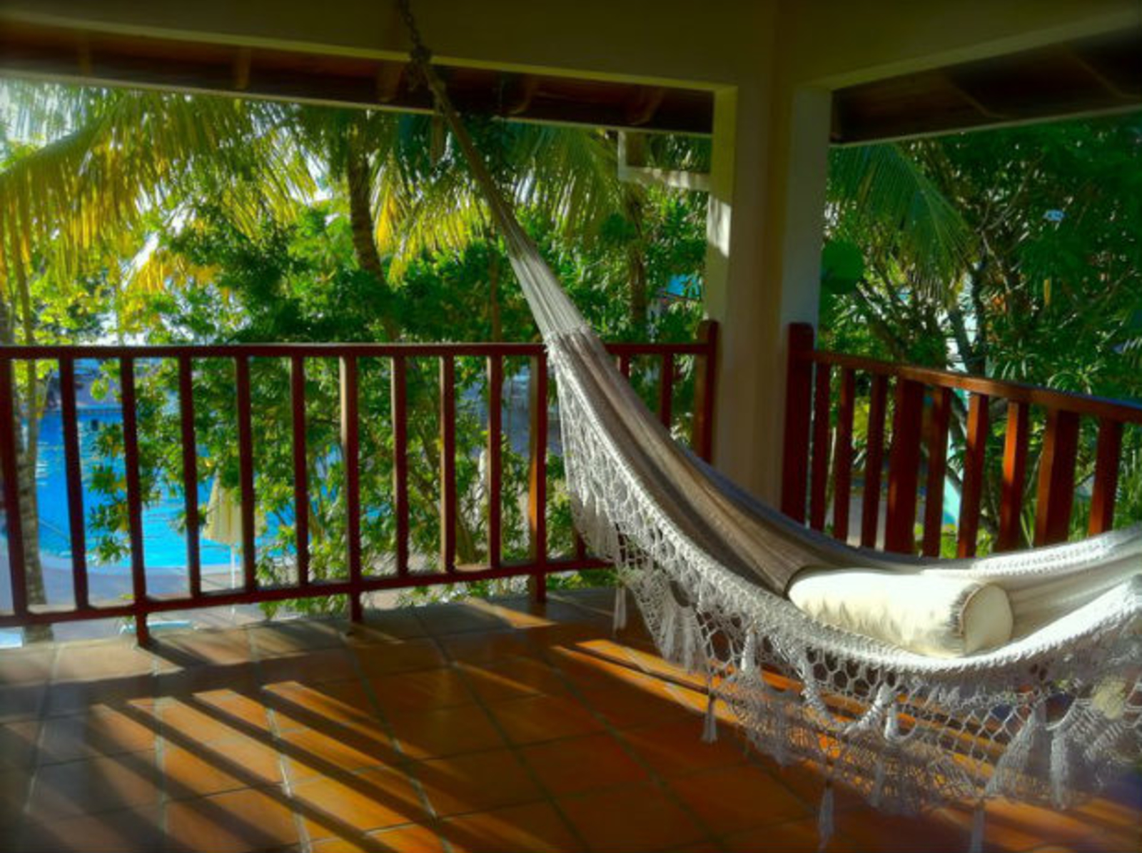 White hammock hanging on a shaded deck surrounded by palm trees