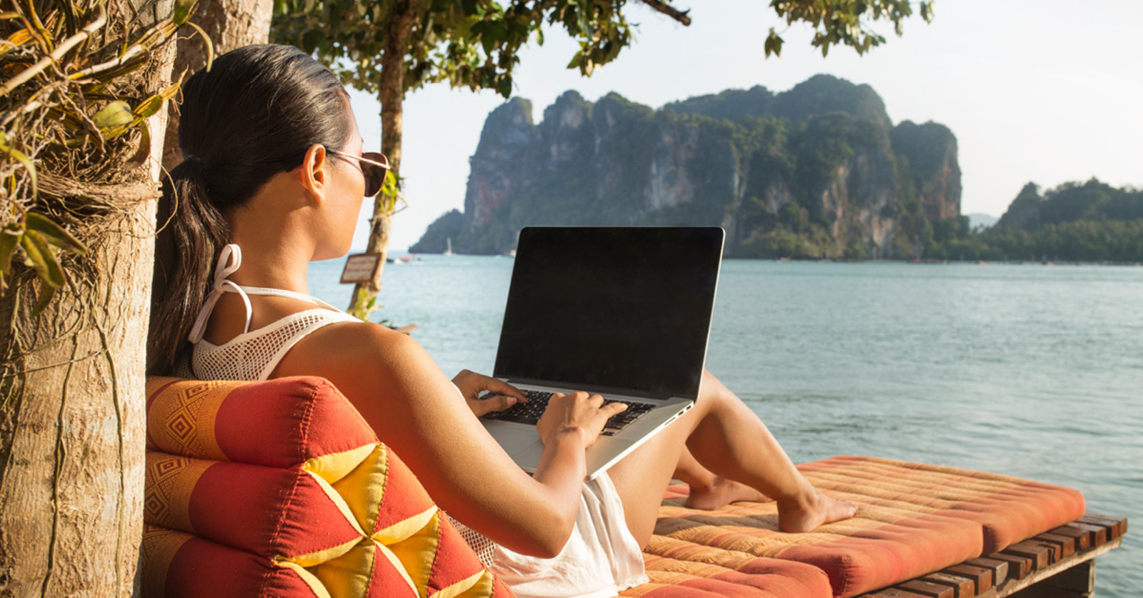 Woman reclining in a chair typing on a blank laptop, with tall jagged islands in the background