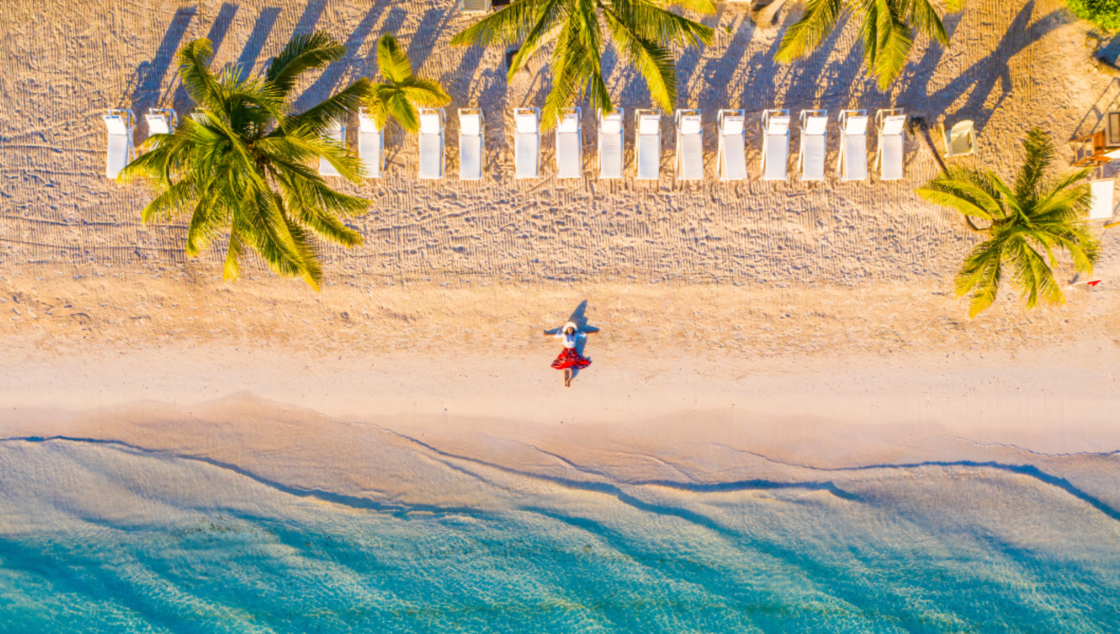 Aerial photo of a woman lying on the beach with beach chairs and palm trees