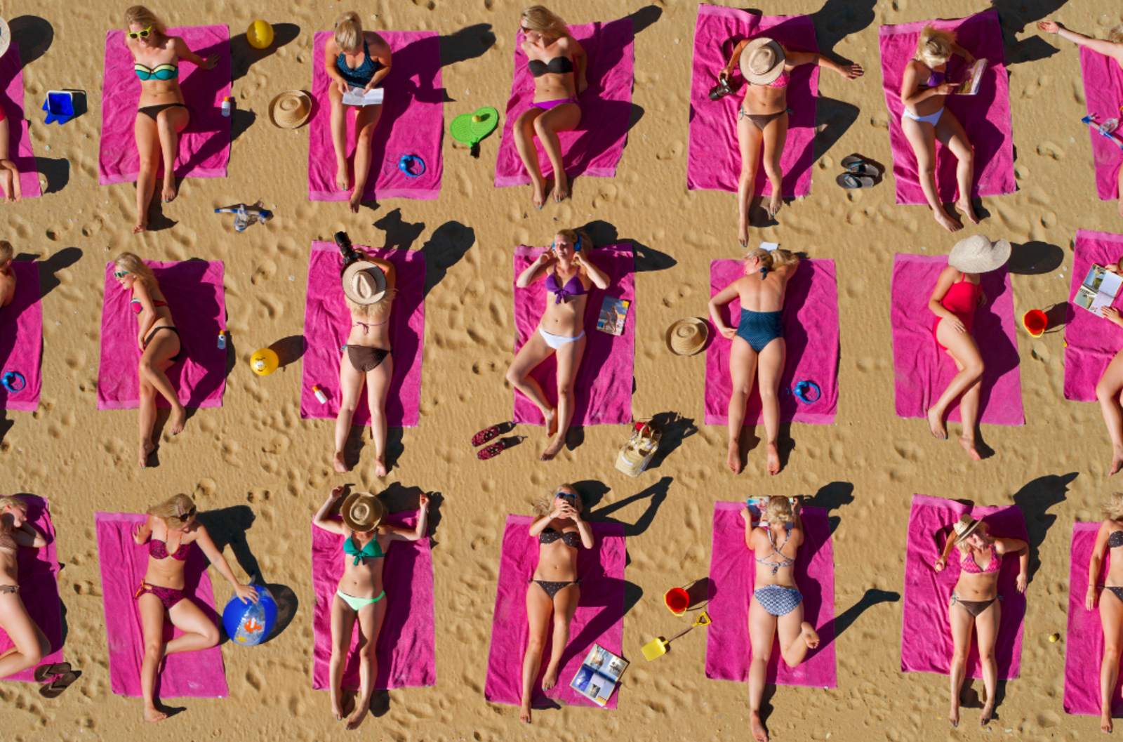 large group of sunbathers lying on pink towels on a beach.
