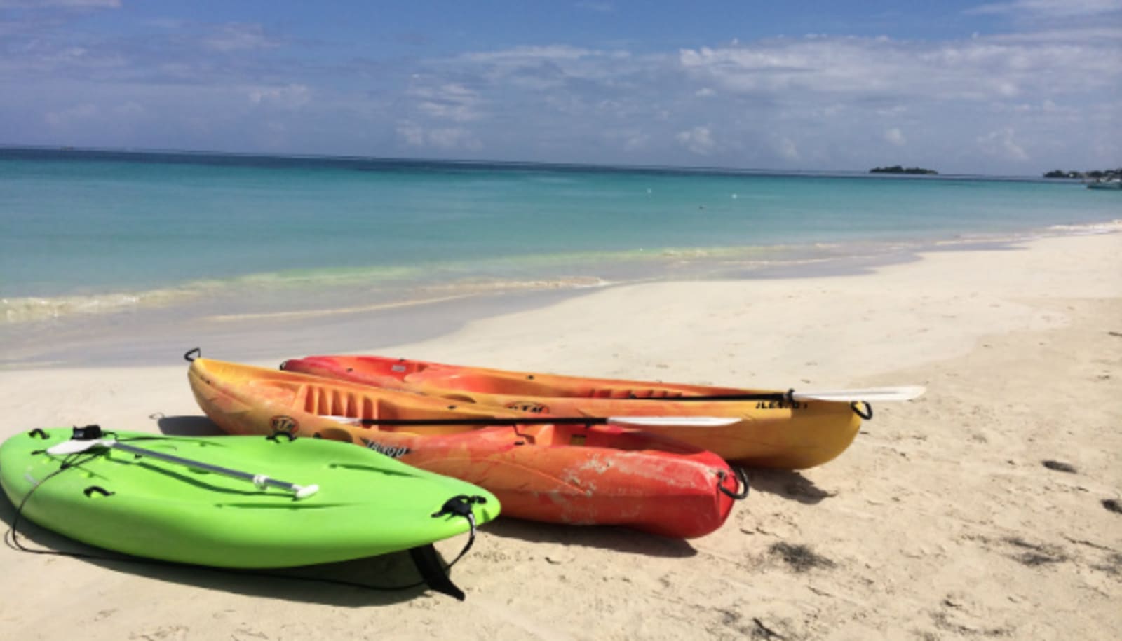Kayaks and stand-up paddleboards on the sand at a clear beach