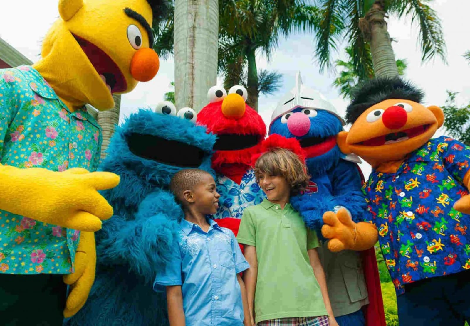 Two kids hangning out with Bert, Cookie Monster, Elmo, Super Grover and Ernie from Sesame Street