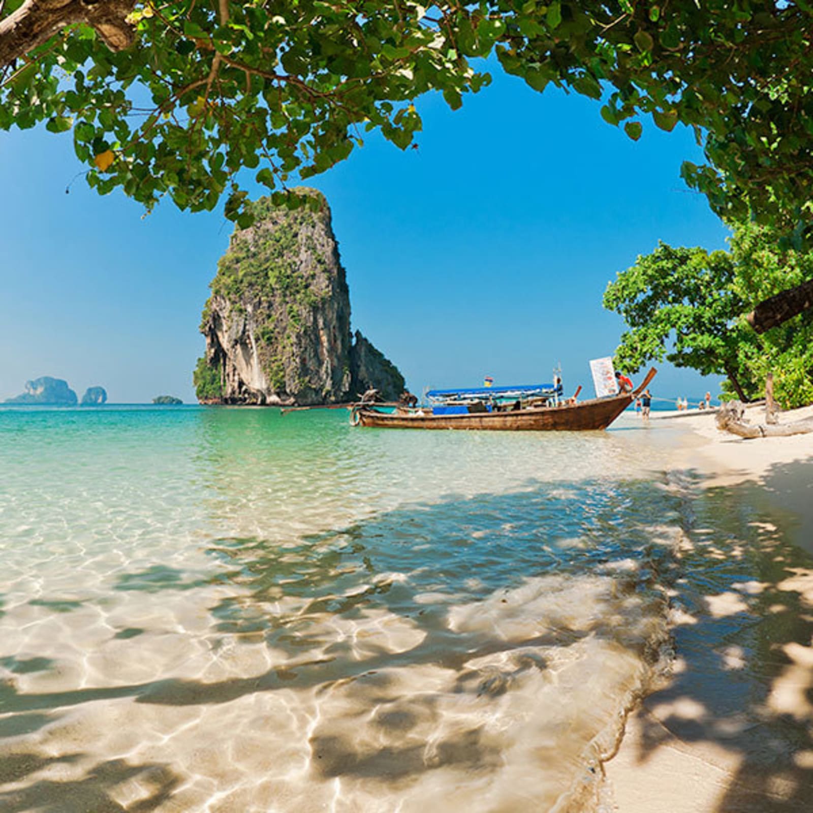 Small boat docked on a beach in Thailand, with a large rock jutting out of the ocean behind