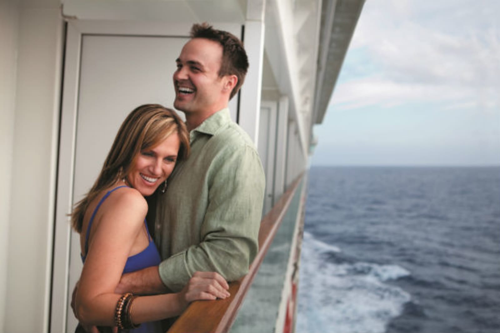 Couple smiling and embracing standing near the ocean-line on a cruise ship