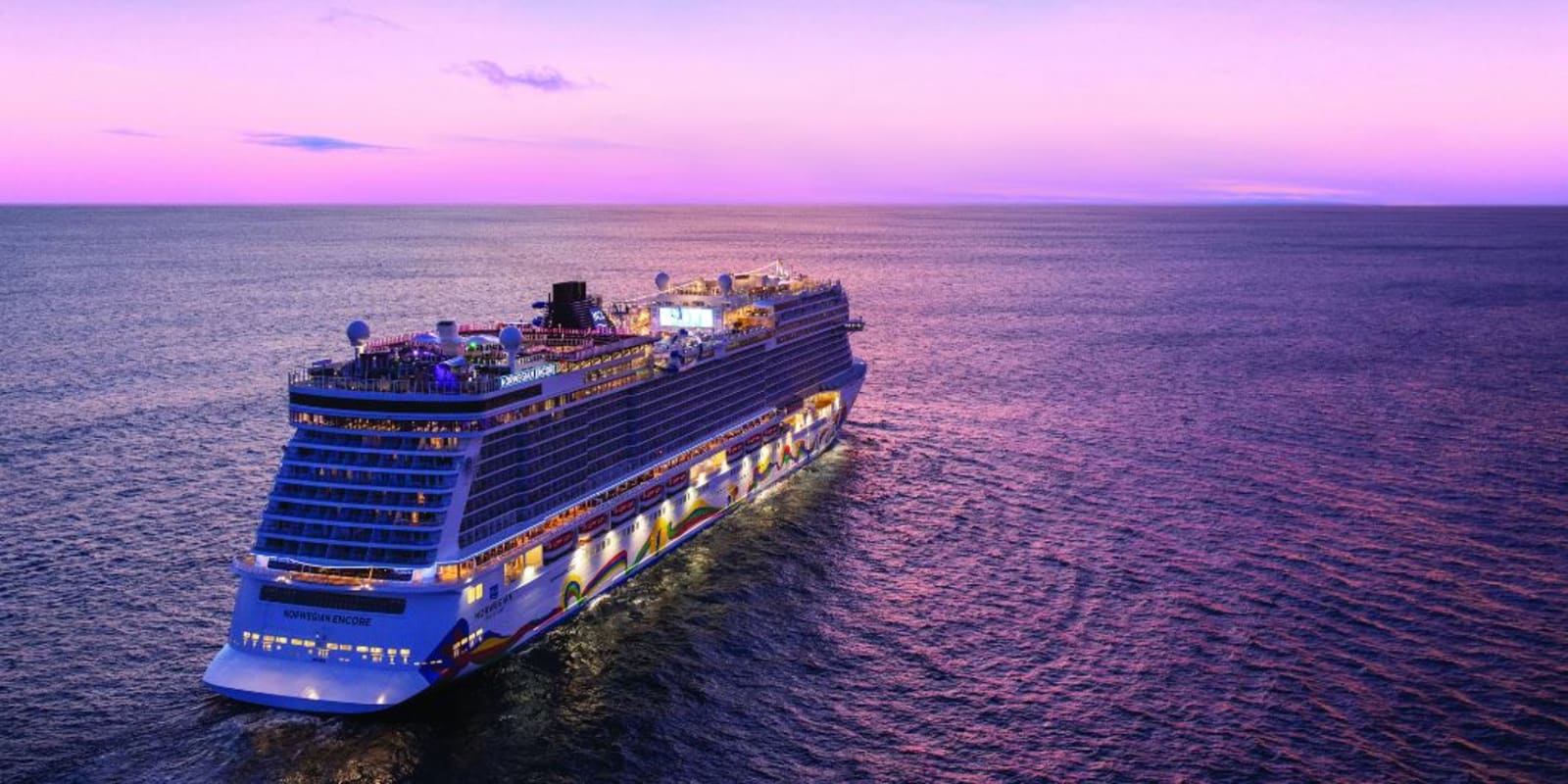 A large cruise ship sailing towards the horizon as the sunset turns the sky pink and purple.