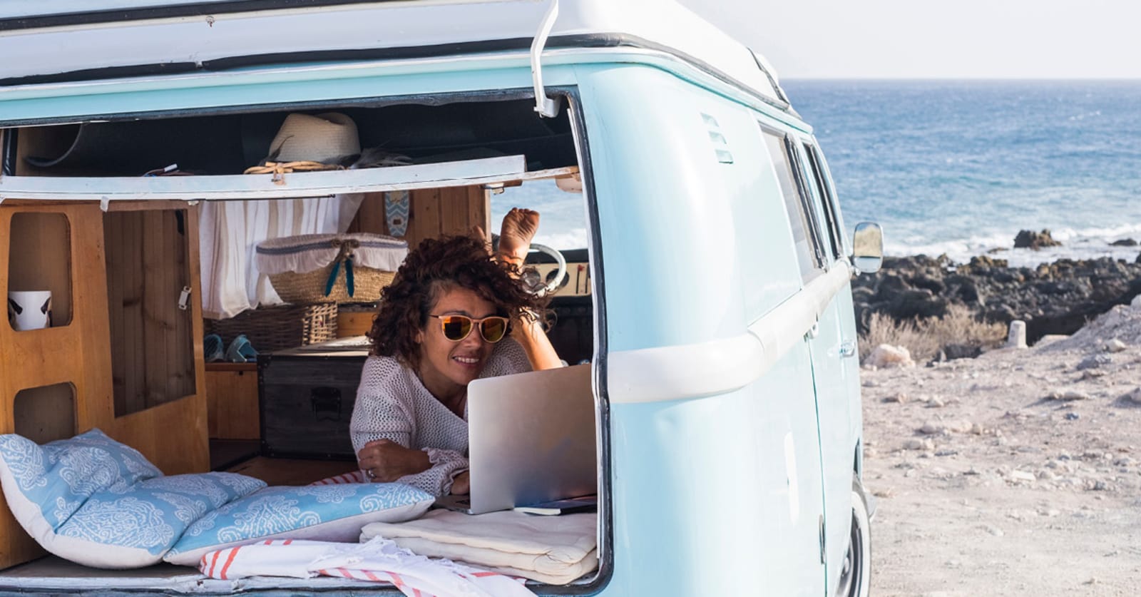 Woman in camper van parked at the beach, looking at her laptop