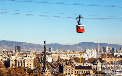 Red cable car travelling over a historic city against a blue sky.