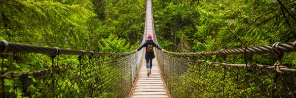 Woman crossing a tall rope bridge in a dense forest