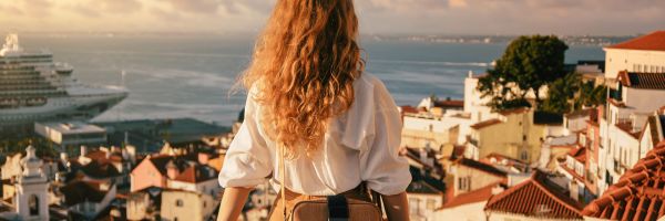 Woman with curly brown hair at a balcony looking over a seaside town