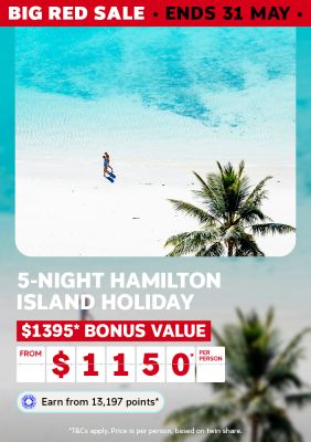 Couple strolling on a white sand Hamilton Island beach beside turquoise water for a 5-night holiday with $1395 bonus value from $1150 per person