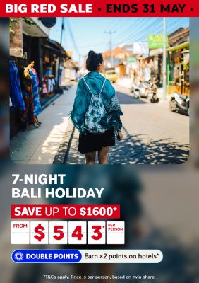Traveller walking through a sunny Bali market street lined with colourful shops for a 7-night holiday saving up to $1600 from $543 per person