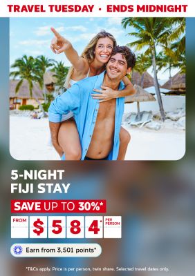 Couple laughing on a piggyback ride along a palm fringed Fiji beach for a Travel Tuesday 5-night stay saving up to 30% from $584 per person