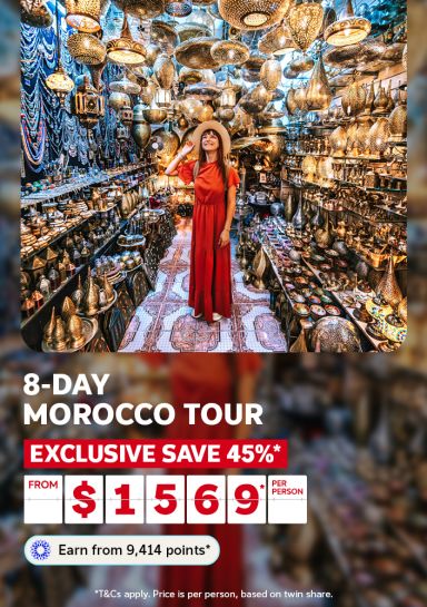 Woman in a red dress marvelling at ornate lanterns and brass wares in a Moroccan souk for an 8-day Morocco tour saving 45% from $1569 per person