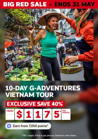 Traveller at a bustling Vietnamese street market trying on a conical hat for a 10-day G Adventures Vietnam tour saving 40% from $1175 per person