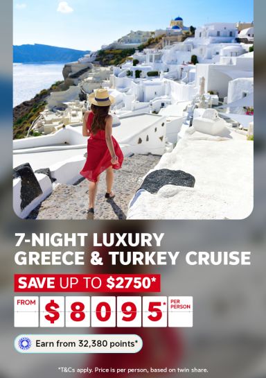 A travel promotional banner featuring a woman in a red dress and straw hat walking along a white-washed stone path overlooking the iconic blue-domed buildings and cliffside scenery of Santorini, Greece. Text reads: "7-Night Luxury Greece & Turkey Cruise – Save up to $2,750* – From $8,095* per person. Earn from 32,380 points*." Fine print states: "T&Cs apply. Price is per person, based on twin share."