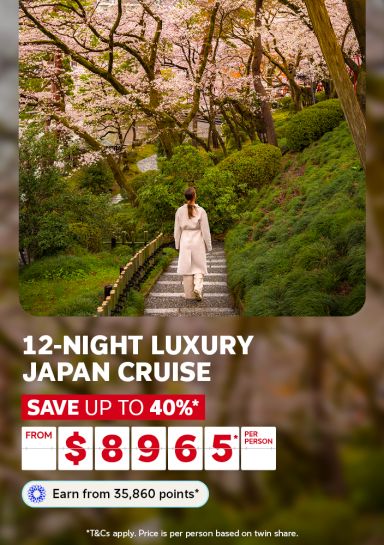 Woman walking down a stone path beneath blooming cherry blossoms for a 12-night luxury Japan cruise saving up to 40% from $8965 per person