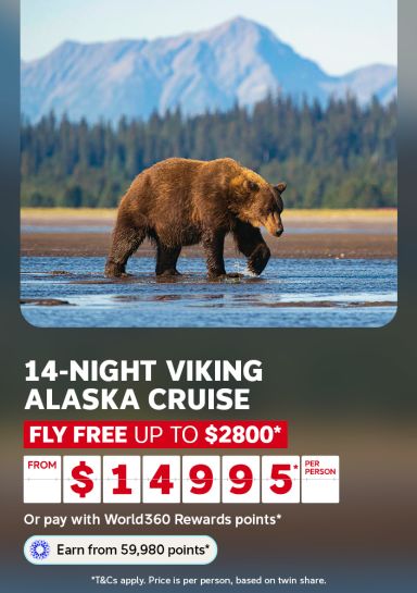 Brown bear wading through shallow water below misty mountains for a 14-night Viking Alaska cruise with fly free up to $2800 from $1495 per person
