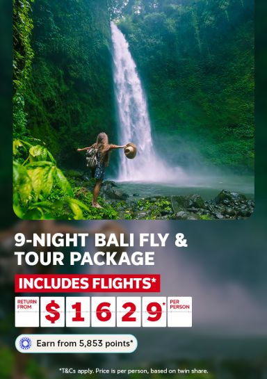 oman with backpack and hat raising arms before a Bali waterfall for a 9 night fly and tour package including flights from $1629 per person