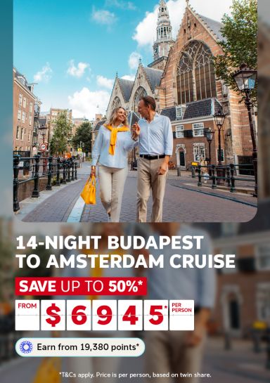 Couple strolling past a gothic church along an Amsterdam street for a 14-night Budapest to Amsterdam cruise saving up to 50% from 6945 per person