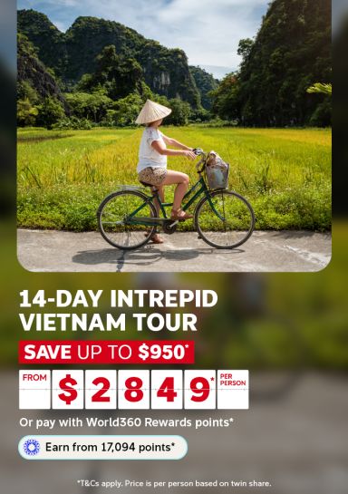 Woman in a conical hat cycling past rice paddies and limestone karsts for a 14-day Intrepid Vietnam tour from $2849 saving up to $950 per person