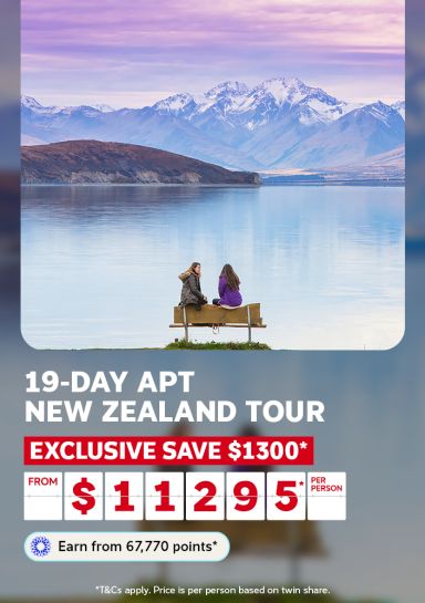 Two people on a lakeside bench gazing at snow-capped peaks for a 19-day APT New Zealand tour with an exclusive saving of $1300 from $11295 per person