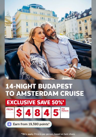 Couple embracing in an open-air vehicle with European architecture behind for a 14-night Budapest to Amsterdam cruise saving 50% from $4845 per person
