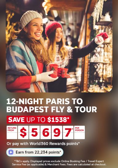 Friends browsing a twinkling Christmas market stall for a 12-night Paris to Budapest fly and tour saving up to 1538 from 5697 per person