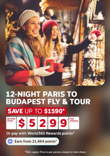 Friends browsing sparkling ornaments at a festive Christmas market for a 12-night Paris to Budapest fly and tour saving up to $1590 from $5299 per person