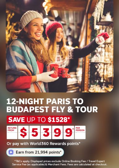 Two friends browsing a Christmas market stall with red mugs for a 12 night Paris to Budapest tour saving up to 1528 dollars from 5399 per person