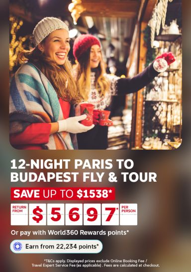 Friends in winter beanies browsing ornaments at a festive Christmas market for a 12-night Paris to Budapest fly and tour from 5697 per person