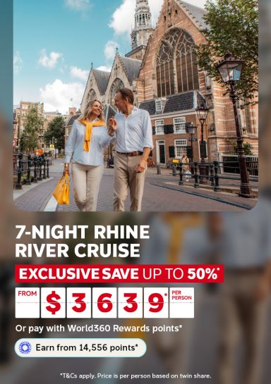 Couple strolling past a historic gothic church in Amsterdam for a 7-night Rhine river cruise saving up to 50% from $3639 per person