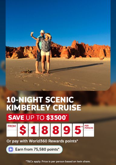 Couple taking a selfie on a red sand beach beneath rugged cliffs for a 10-night Scenic Kimberley cruise saving up to $3500 from $1895 per person
