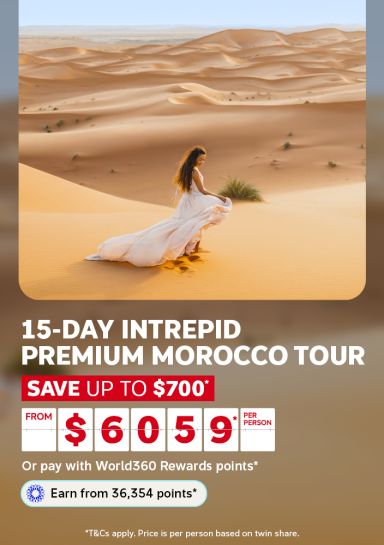 Woman in a flowing dress walking among golden Sahara sand dunes for a 15-day Intrepid premium Morocco tour saving up to $700 from $6059 per person