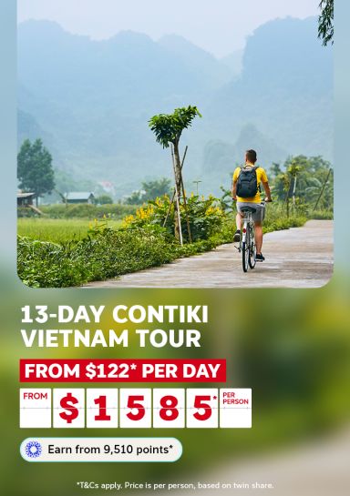 Cyclist riding a rural path beneath misty limestone mountains in Vietnam for a 13-day Contiki tour from $122 per day