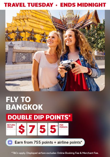 Two women smiling holding a camera in front of a golden temple in Thailand featuring flights to Bangkok return from $755* per person