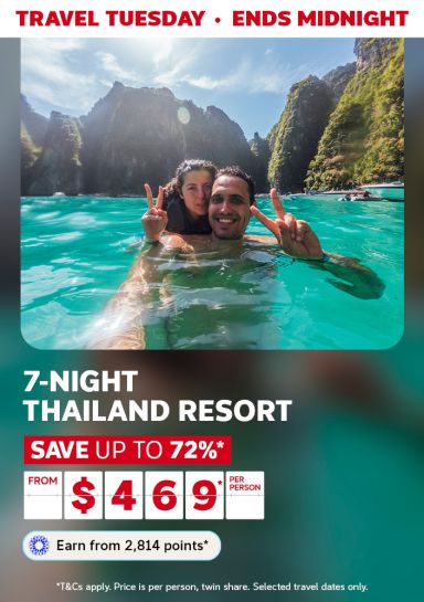 Couple making peace signs in turquoise water below limestone cliffs for a Travel Tuesday 7-night Thailand resort saving up to 72% from 469 per person