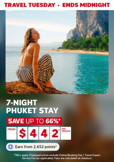 Woman smiling, looking out at the ocean and a tall limestone cliff featuring a 7-night Phuket stay from $442