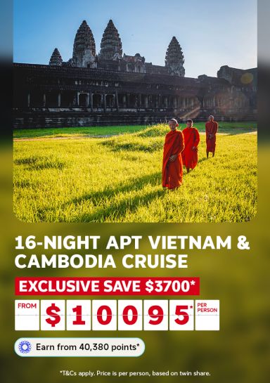 Monks in saffron robes on sunlit grounds before the ancient towers of Angkor Wat for a 16-night APT Vietnam and Cambodia cruise saving $3700 from $10095