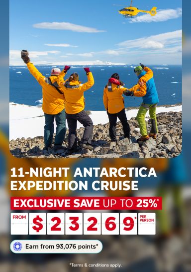 Travelers celebrating on a rocky Antarctic shore as a helicopter flies overhead for an 11-night expedition cruise saving up to 25% from $2369 per person