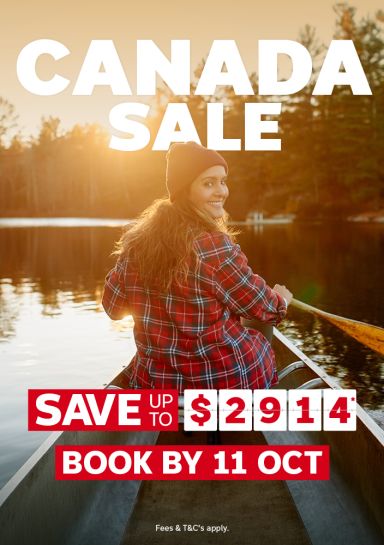 Woman in a plaid shirt and beanie smiling back while canoeing a golden sunset lake for the Canada sale saving up to 2914 book by 11 October