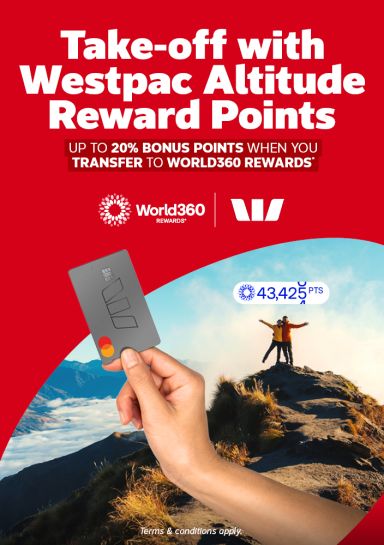 Hand holding a Westpac Altitude card beside travellers celebrating atop a mountain summit for up to 20 percent bonus World360 Rewards points