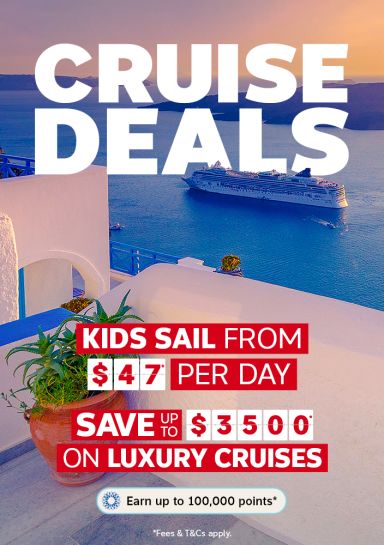 Cruise ship sailing past white-washed Santorini buildings and blue domes at sunset for cruise deals with kids sailing from $47 per day and savings up to $3500 on luxury cruises