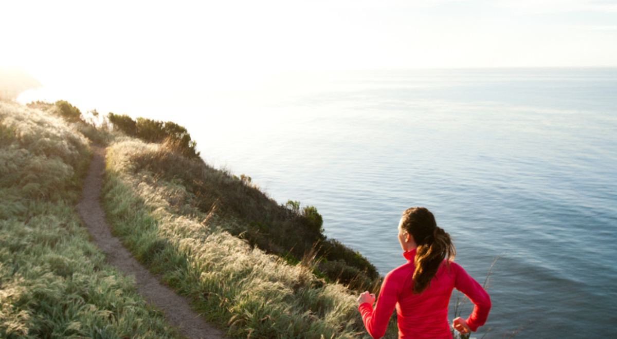 a woman in pink jacket running through the terrain by the river