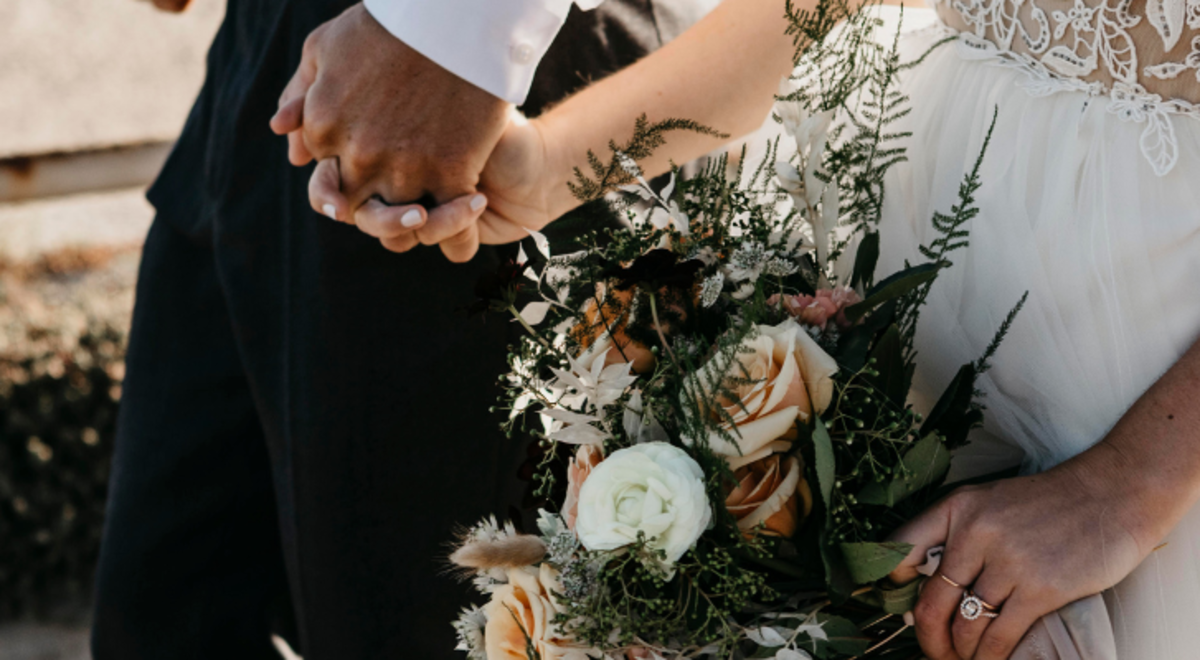 A close up of a bride and groom holding hands