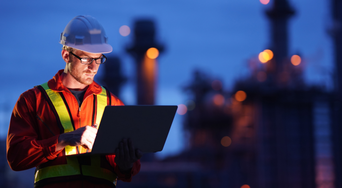 An engineer works on a laptop in the dark at an oil and gas plant